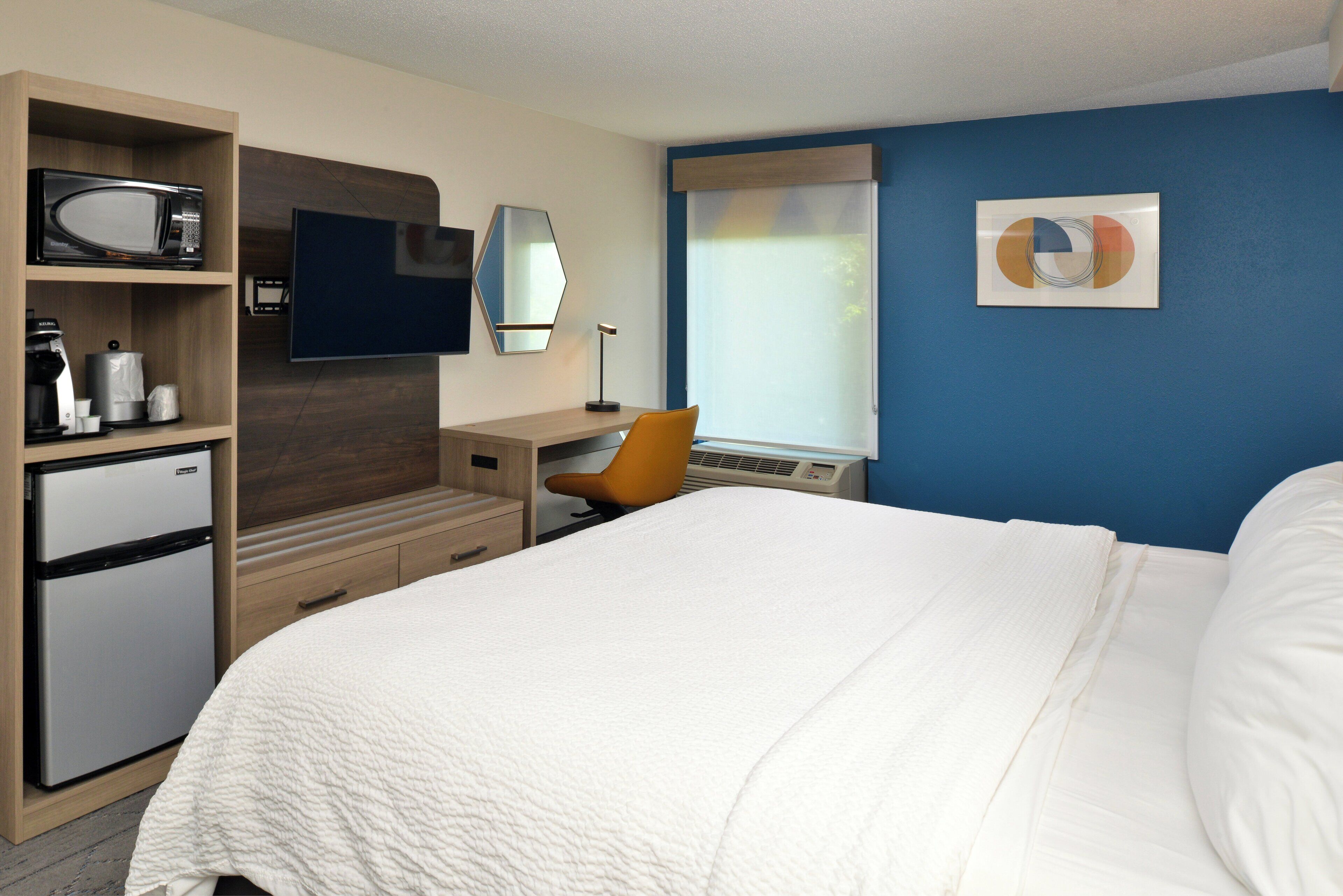A hotel room with a bed, a desk, a chair, a television, a refrigerator, and a coffee maker.