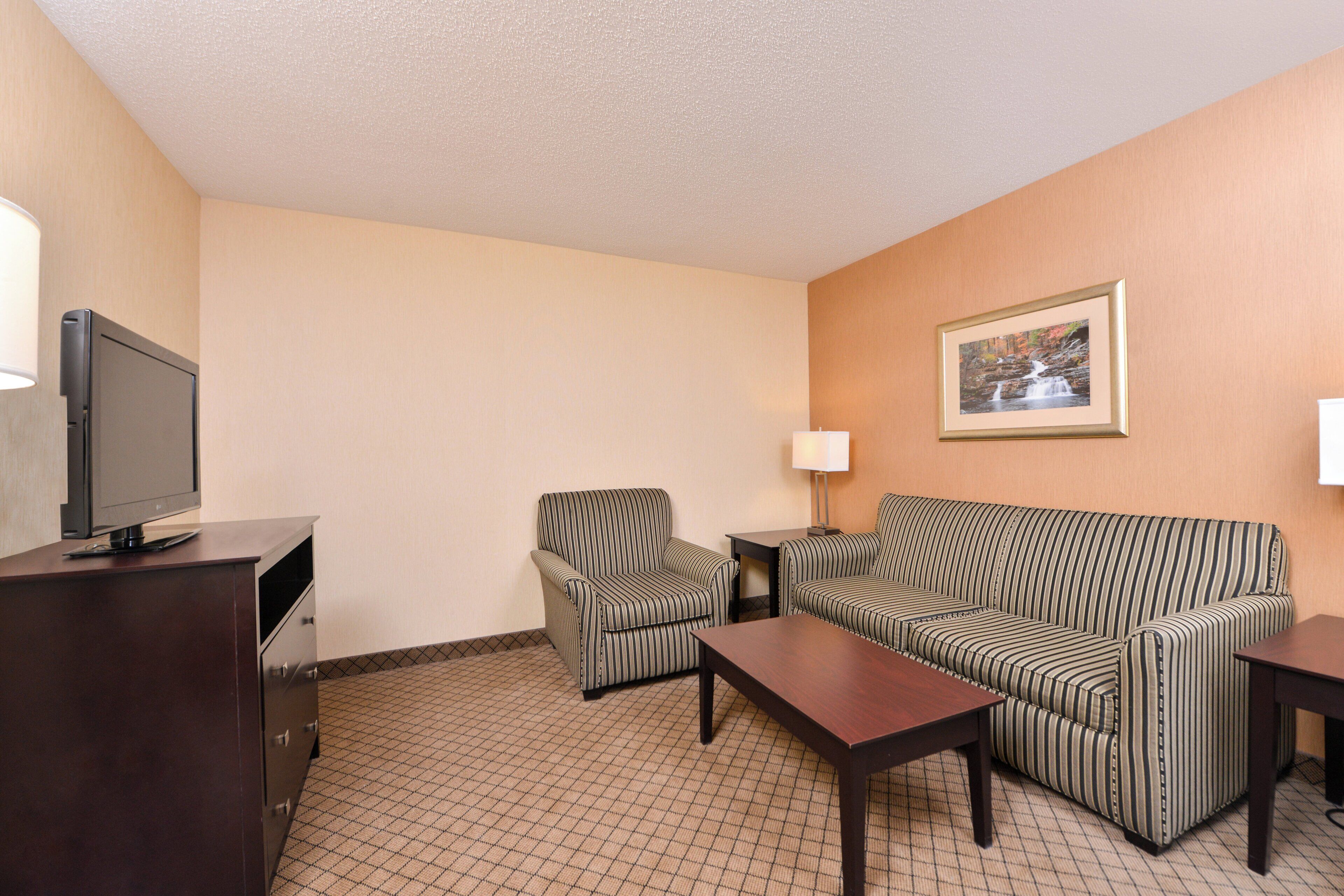 A hotel room with a sofa, armchair, TV, and a framed picture on the wall.