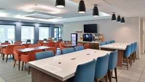 A modern dining area with multiple tables and chairs, a coffee machine, and a flat-screen TV on the wall. - Holiday Inn Express Lewisburg/New Columbia by IHG (New Columbia)