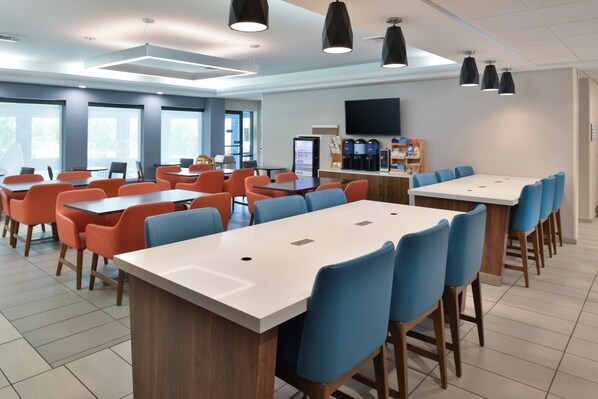 A modern dining area with multiple tables and chairs, a coffee machine, and a flat-screen TV on the wall. - Holiday Inn Express Lewisburg/New Columbia by IHG (New Columbia)