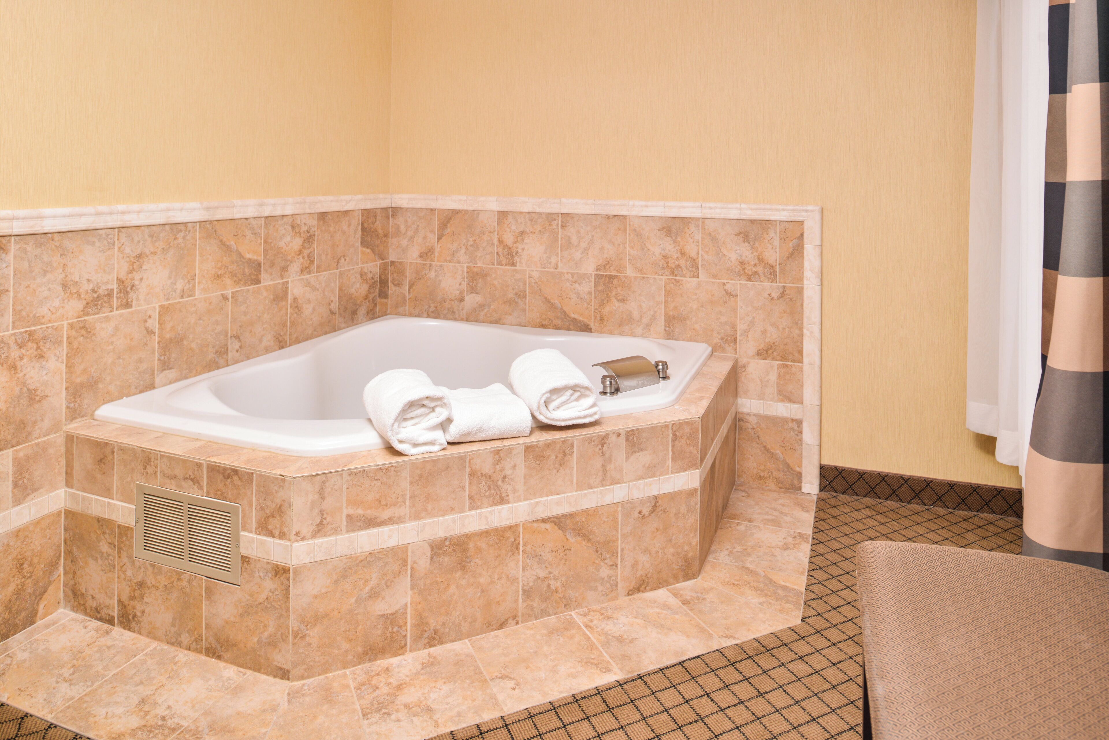 Ein Badezimmer im Eckbereich mit einer freistehenden Badewanne, einem Handtuchhalter und einem Lüftungsgitter.