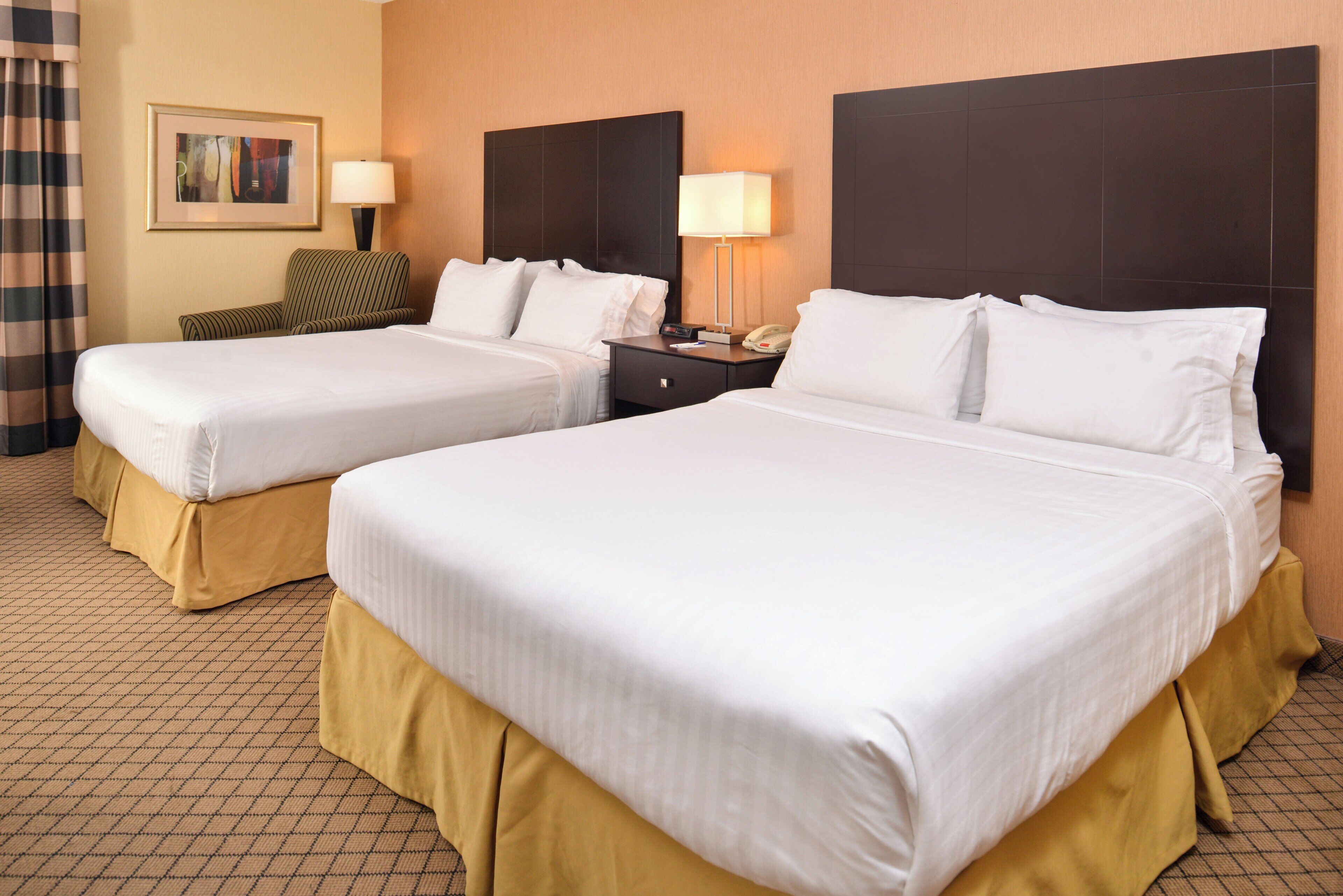 A hotel room with two beds, a nightstand, a lamp, a telephone, and a framed picture on the wall.