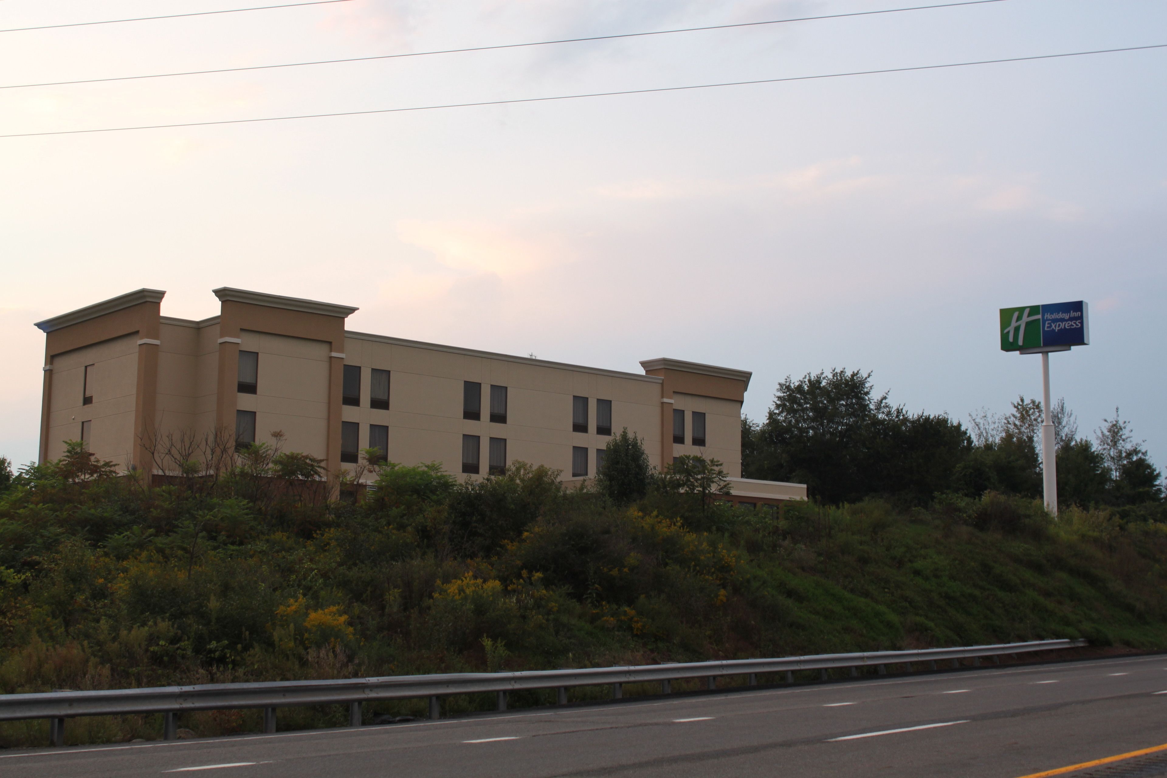 A large, modern building with a flat roof and multiple windows, located beside a highway.