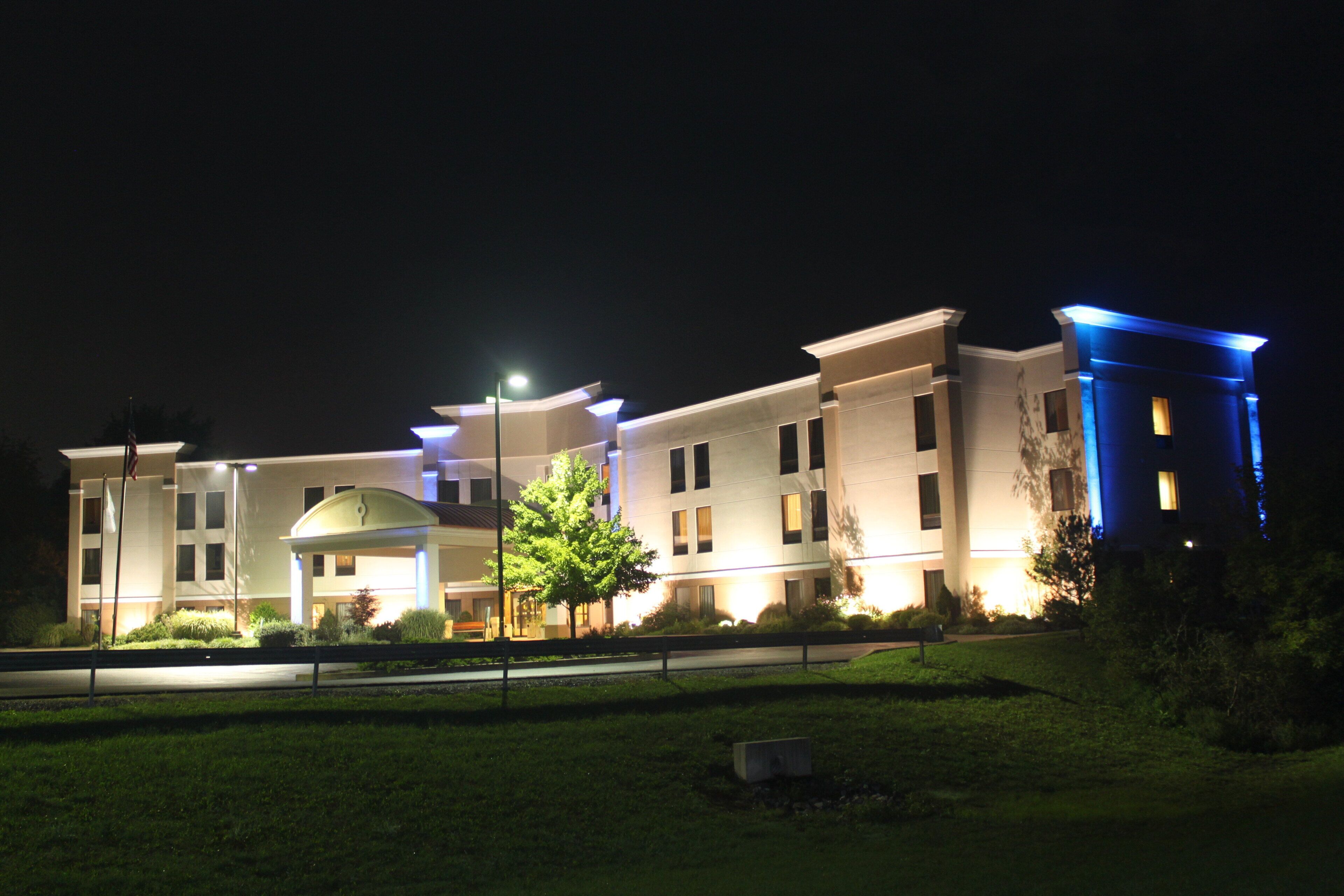 Un hotel de varios pisos con un patio central, un asta de bandera y una entrada bien iluminada.