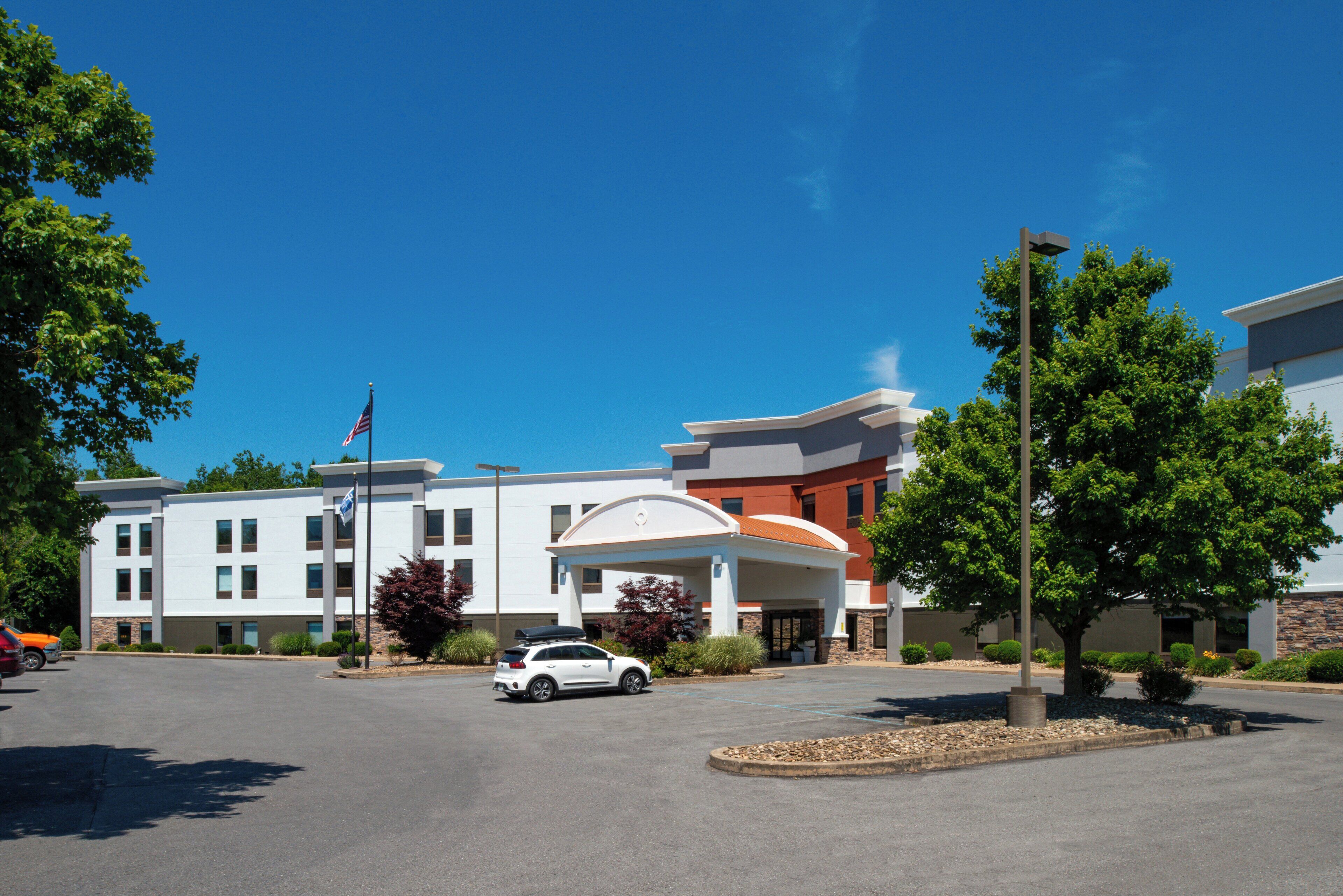 A multi-story hotel with a central entrance, a parking lot, and surrounding greenery.