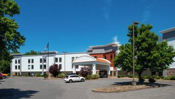 A multi-story hotel with a central entrance, a parking lot, and surrounding greenery.