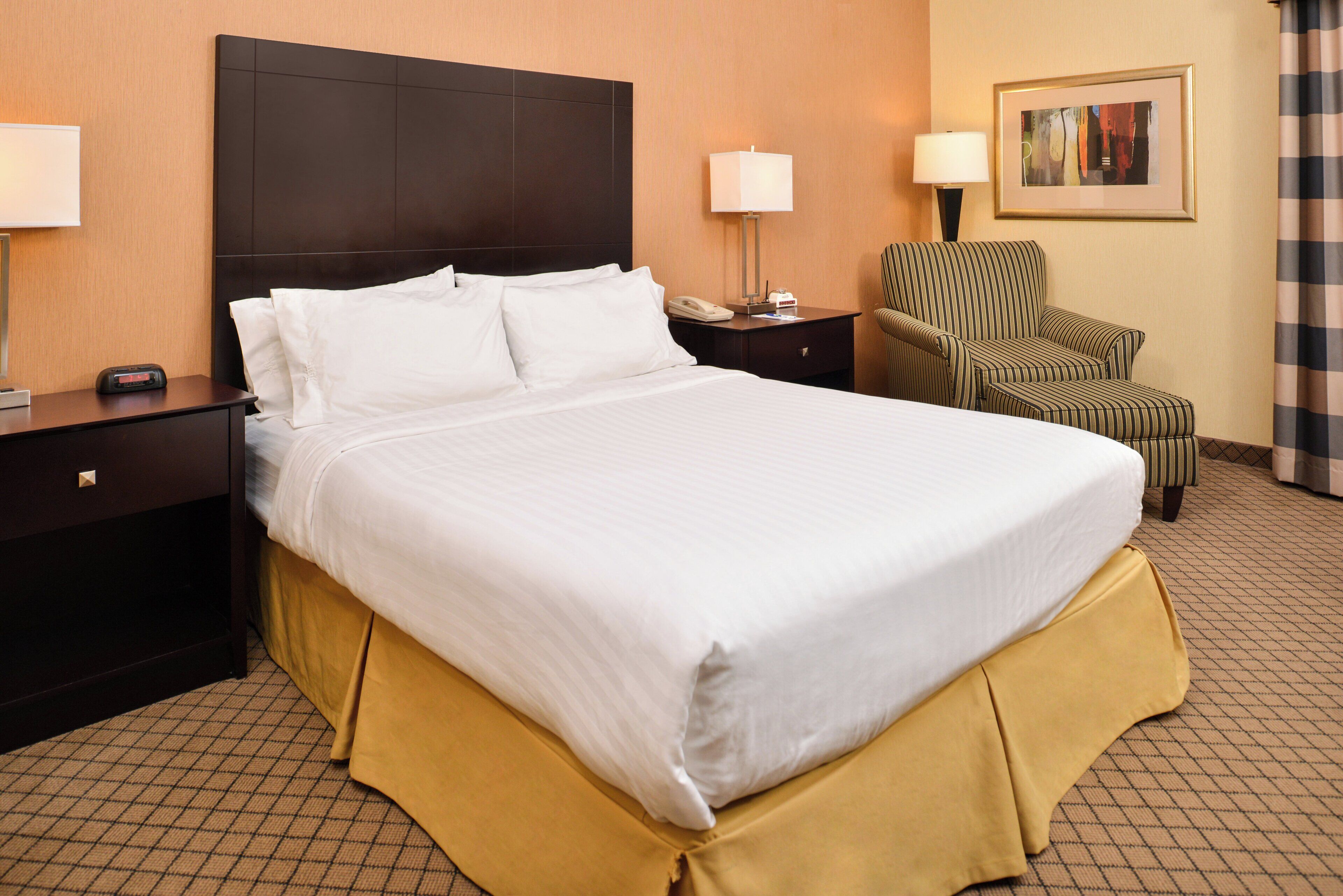 A hotel room with a large bed, a chair, a nightstand, and a lamp.