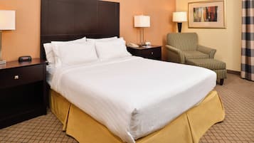 A hotel room with a large bed, a chair, a nightstand, and a lamp.