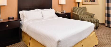 A hotel room with a large bed, a chair, a nightstand, and a lamp.
