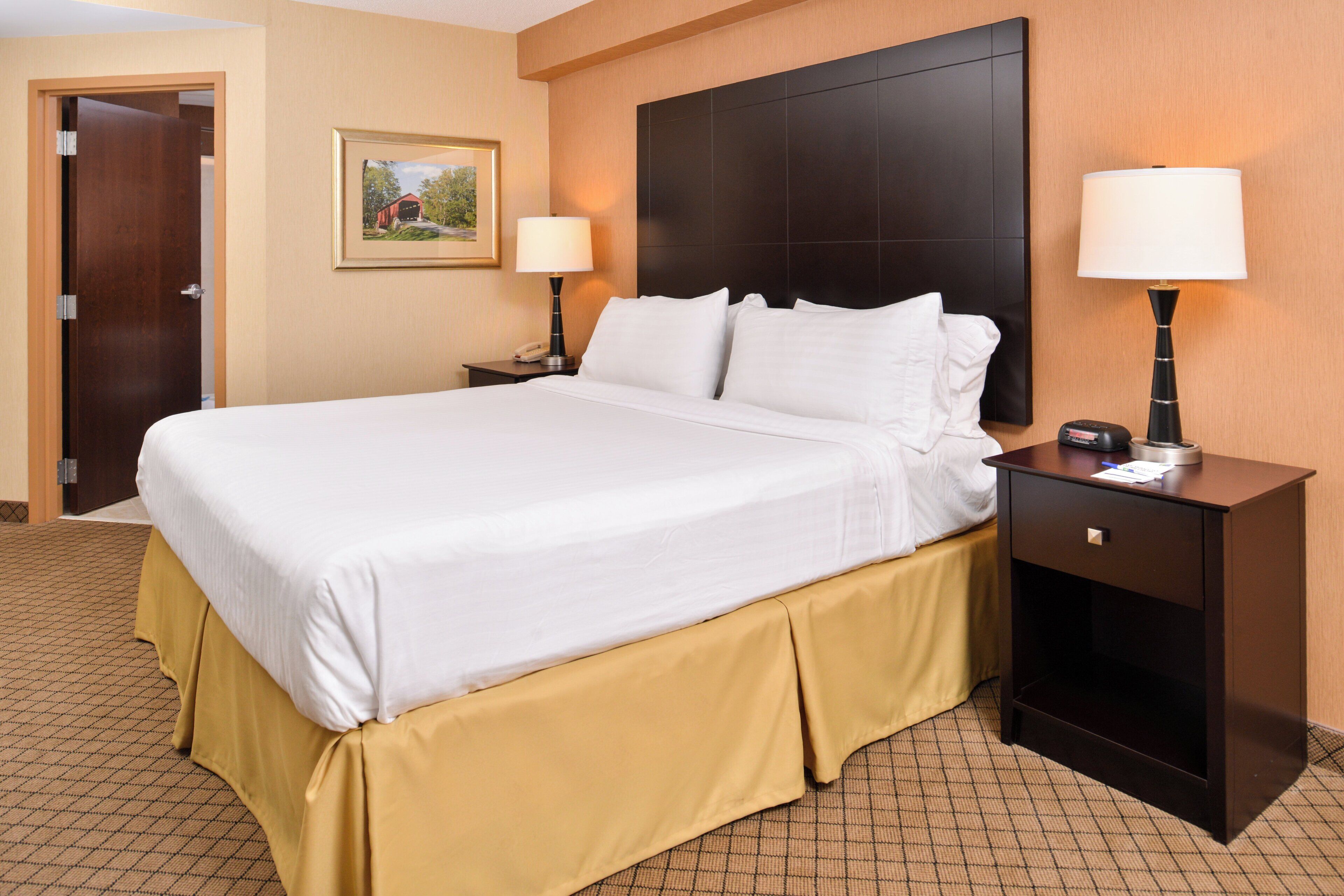 A hotel room with a large bed, two bedside tables, a nightstand, a wall-mounted TV, and a door.