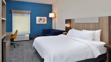 A hotel room with a large bed, a desk, a chair, and a wall-mounted lamp.