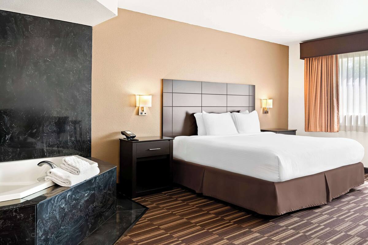 A hotel room with a large bed, a separate bathroom with a bathtub, and a modern design.