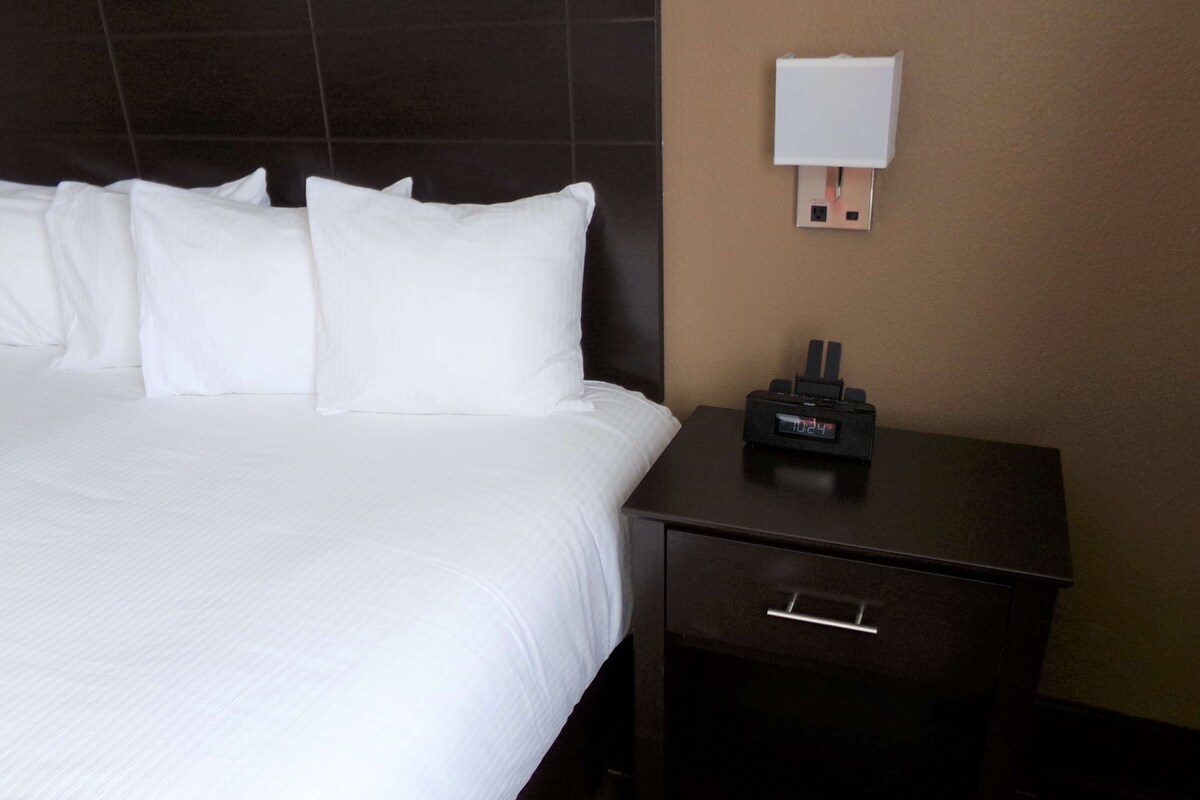 A hotel room with a large bed, a bedside table with a clock, and a wall socket.