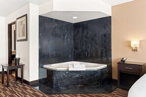 A modern bathroom with a freestanding bathtub, a small table with a bucket, and a bedside table with a lamp. - Best Western Monticello Gateway Inn (Monticello)