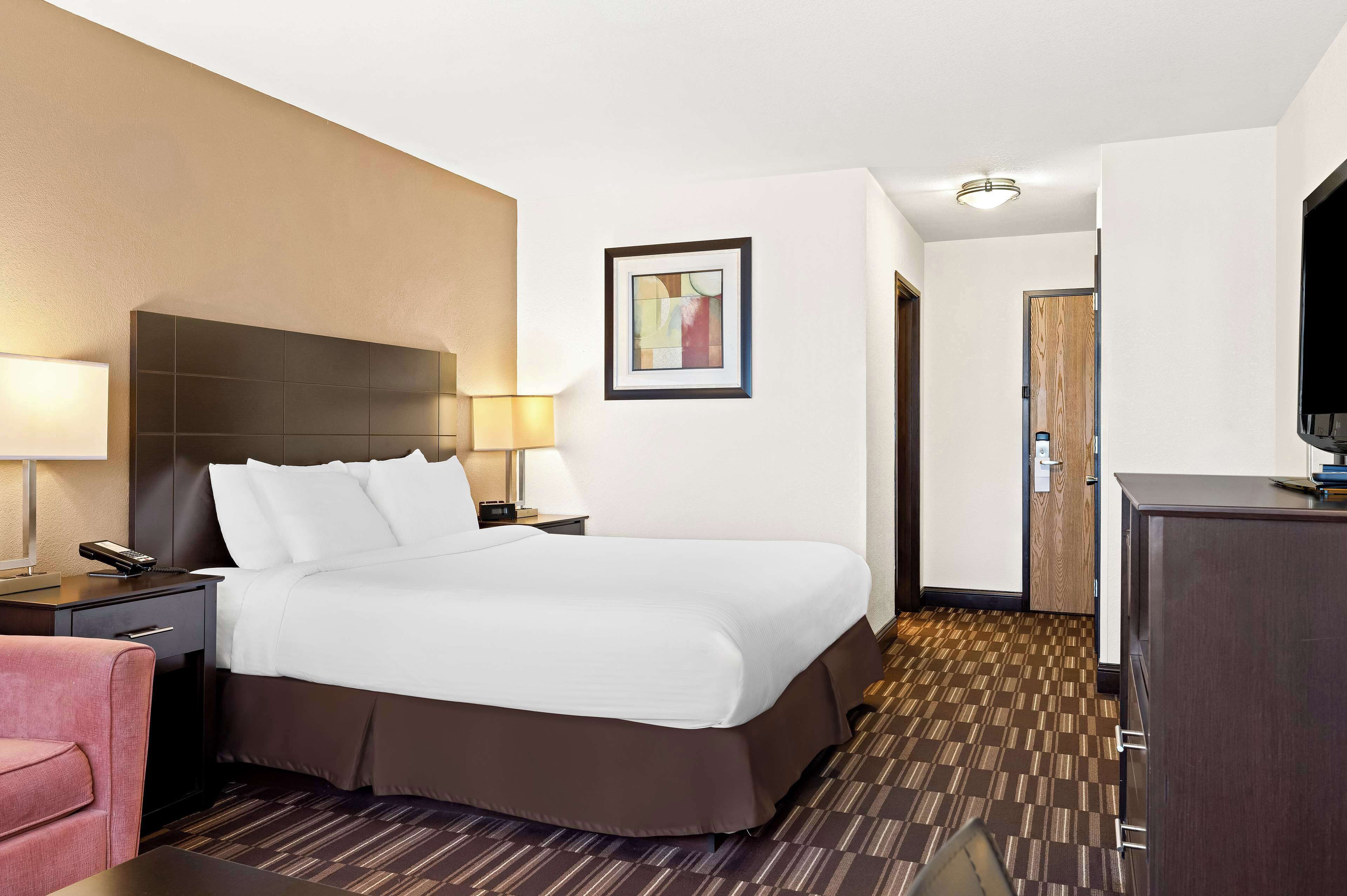 A hotel room with a large bed, a desk with a lamp, a chair, and a television on a cabinet.