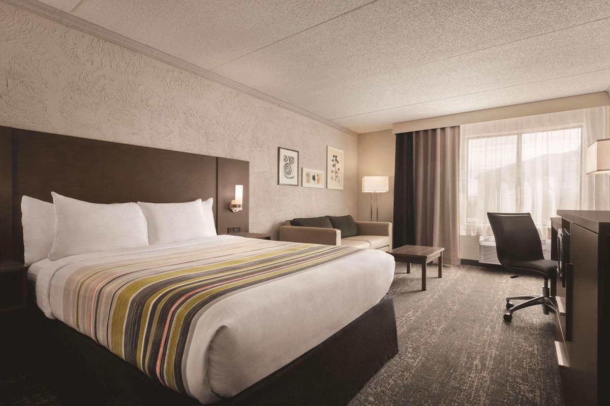 Quarto de hotel com uma cama grande, uma escrivaninha, uma cadeira e um sofá.