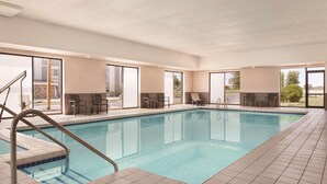 An indoor swimming pool with clear blue water, surrounded by tiled flooring and equipped with a metal ladder.