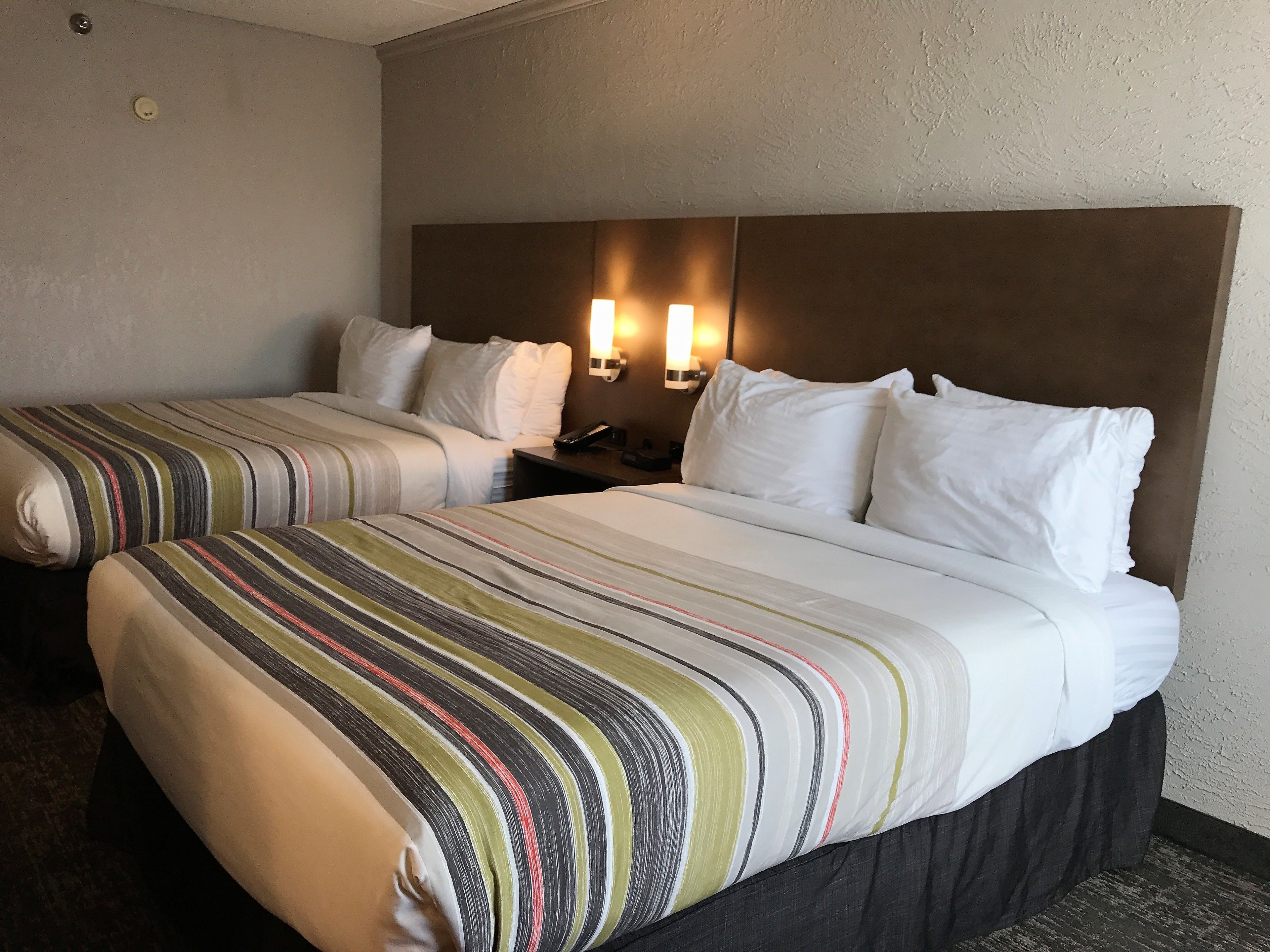 A hotel room with two beds, a headboard, bedside lamps, and a telephone.