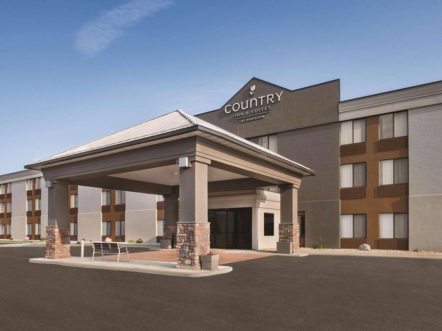 Edificio de Country Inn & Suites con un porche cubierto, varios pisos y un estacionamiento.