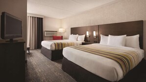 A hotel room with two beds, a television, a lamp, and a wall-mounted air conditioner.