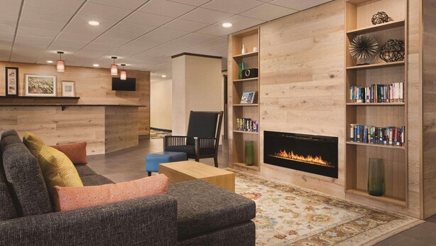A modern living room with a fireplace, a sofa, a bookshelf, and a coffee table. - Country Inn & Suites by Radisson, Mt. Pleasant-Racine West, WI (Mount Pleasant)