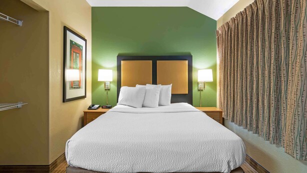 A hotel room with a large bed, green walls, and a patterned curtain.