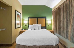 A hotel room with a large bed, green walls, and a patterned curtain.
