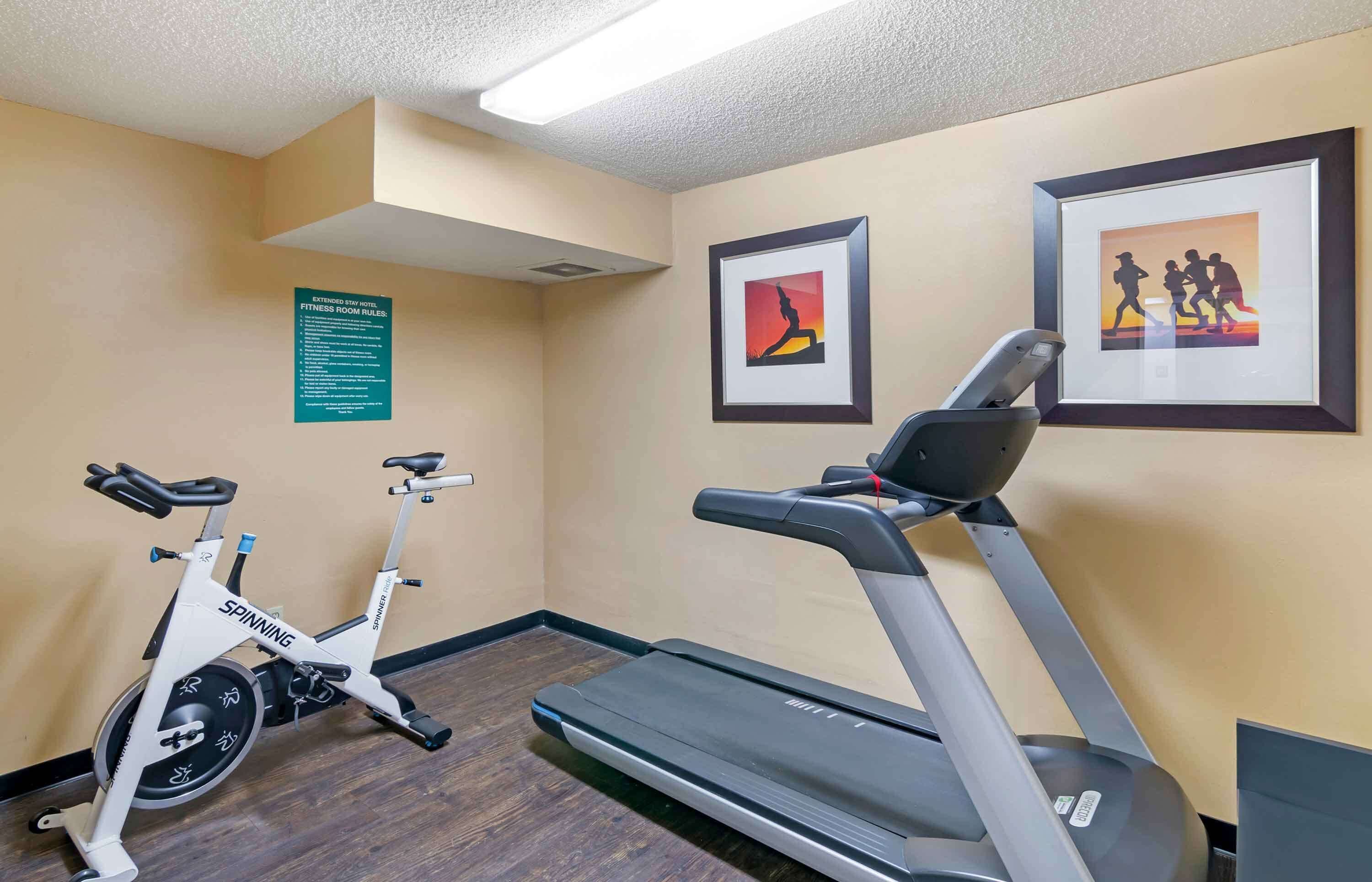 Gimnasio con cinta de correr, bicicleta estática y un cartel en la pared.