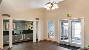 A spacious lobby with a reception desk, a staircase leading to an upper floor, and an exit sign.
