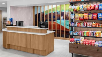 Een hotel receptie met een houten balie, een digitaal scherm en een snackwand.