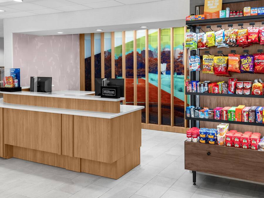 Een hotel receptie met een houten balie, een digitaal scherm en een snackwand.
