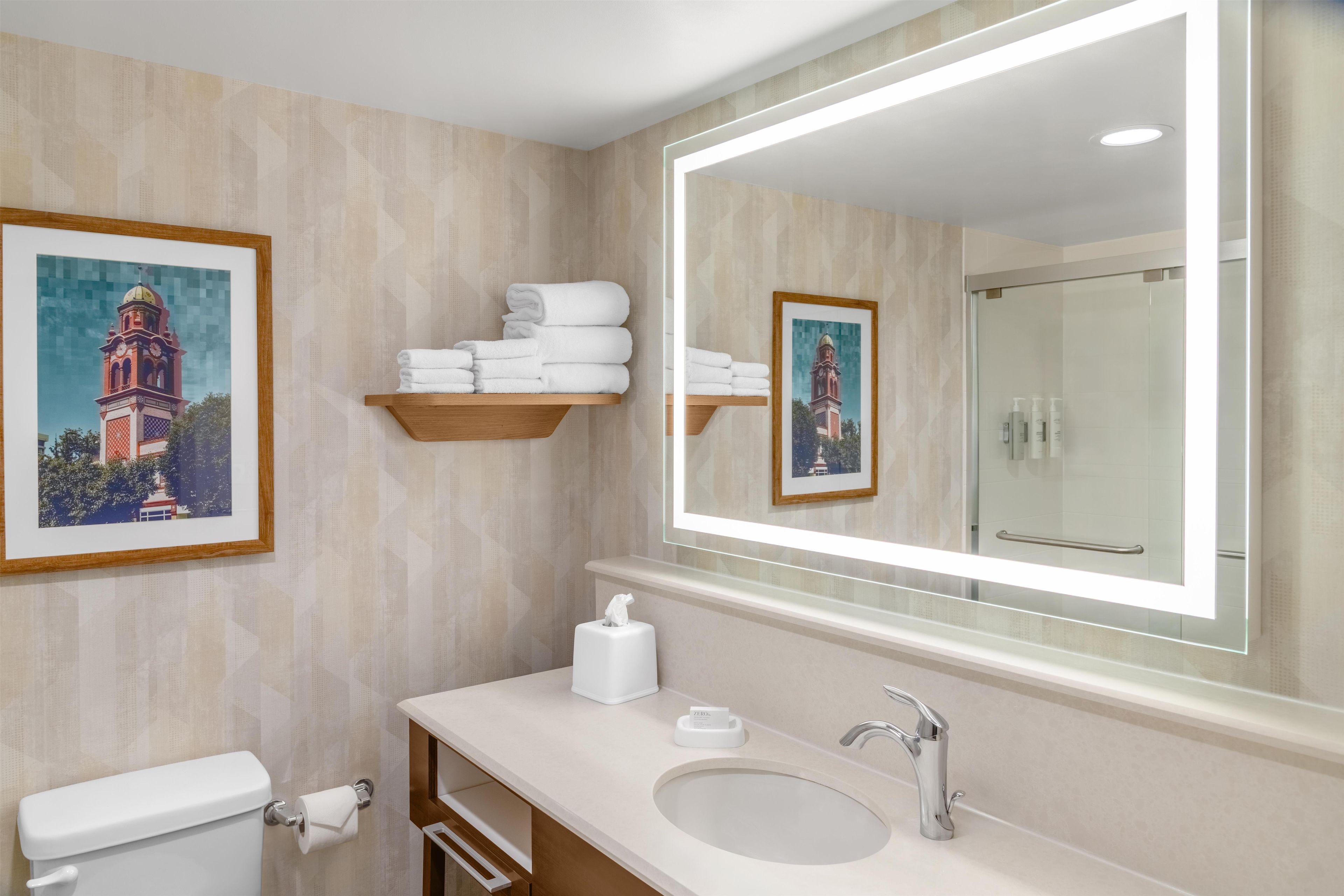 Un baño de hotel con un espejo grande, un lavamanos, un inodoro y un perchero para toallas.