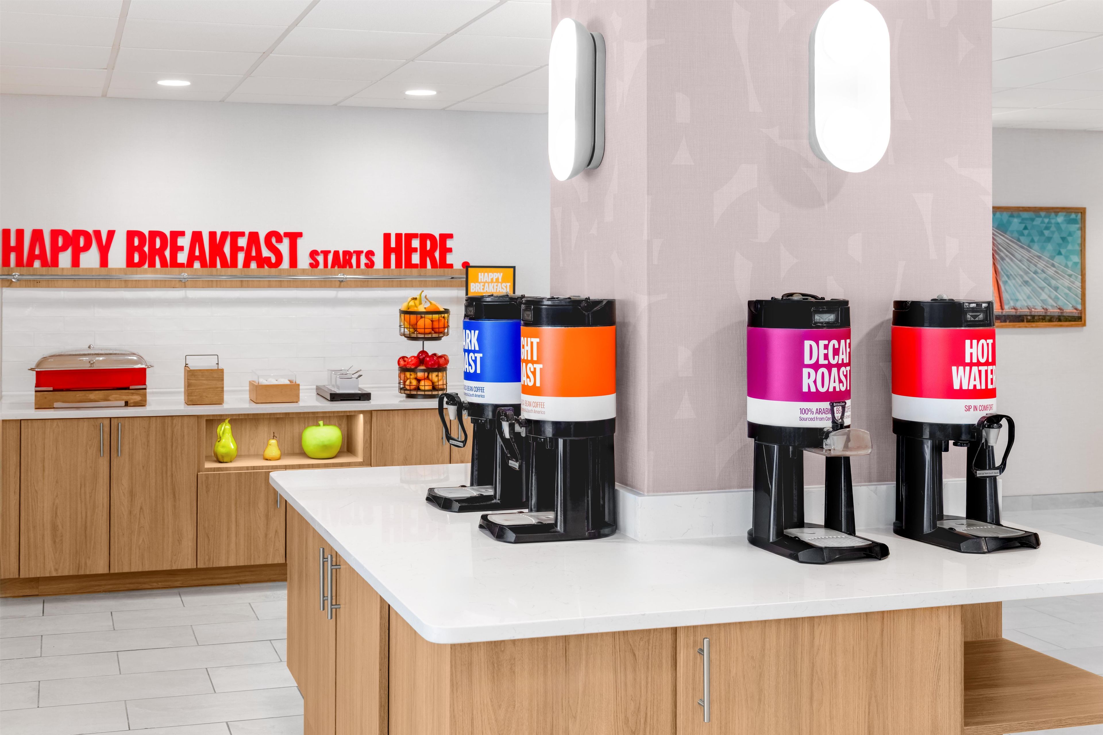 Una barra de desayuno con máquinas de café y un cartel que dice 'HAPPY BREAKFAST STARTS HERE'.