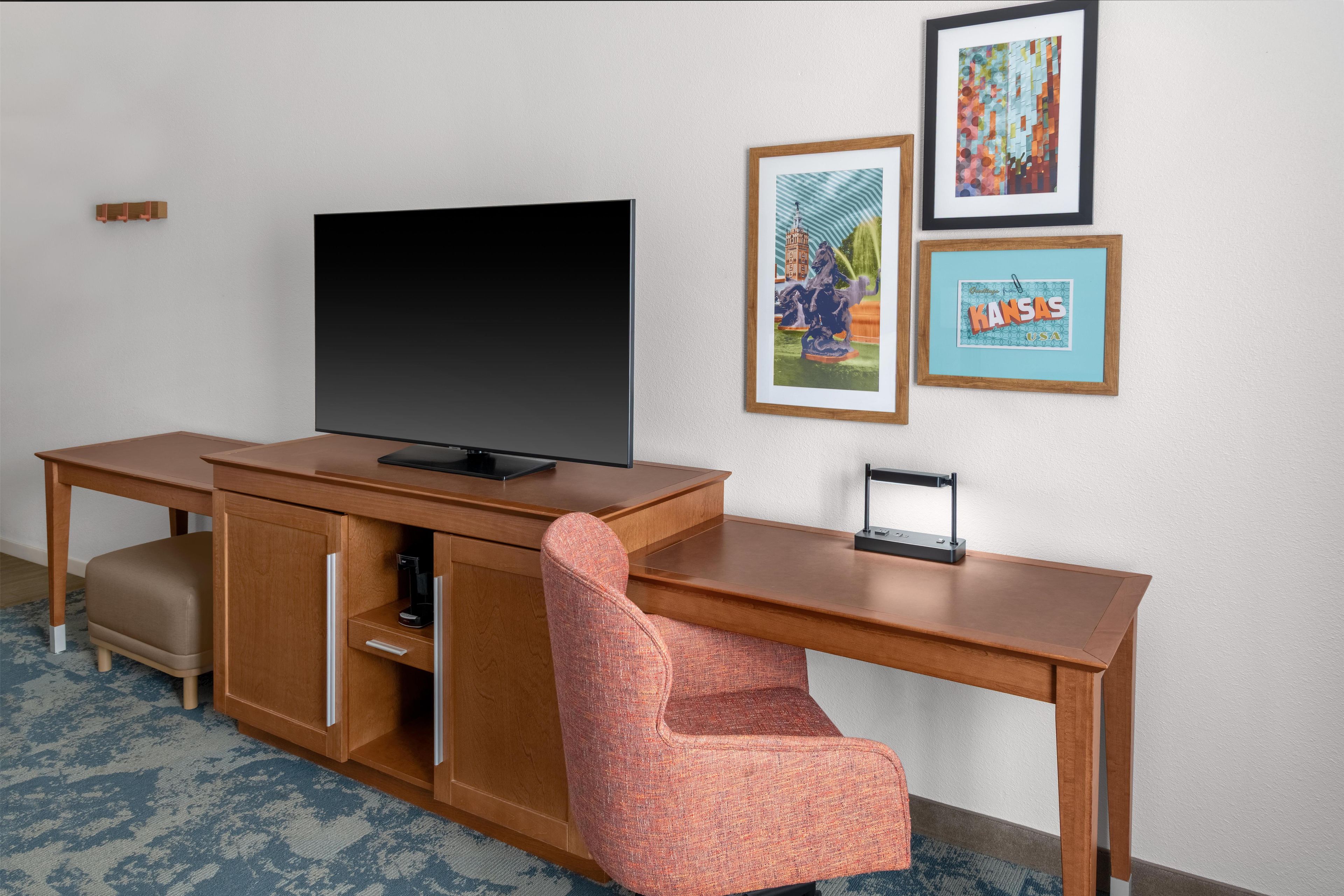 Ein Hotelzimmer mit einem Holztisch, einem Fernseher, einem Stuhl und drei gerahmten Bildern an der Wand.
