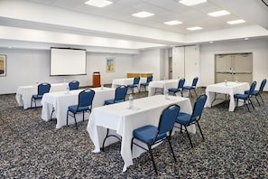 Un salón de conferencias con varias mesas y sillas, una pantalla de proyector y un dispensador de agua.
