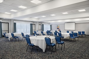 Un salón de conferencias con mesas redondas, sillas azules y una pantalla para proyector.