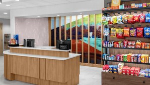 Un espace d’accueil d’hôtel avec un comptoir en bois, un écran numérique et un présentoir de collations.