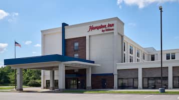 Un hotel Hampton Inn by Hilton con cielo despejado, una bandera estadounidense y un estacionamiento.