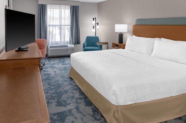A hotel room with a bed, a desk, a chair, a TV, a lamp, and a window with curtains.