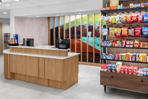 Zona de recepción de un hotel con mostrador de madera, pantalla digital y exhibición de aperitivos.