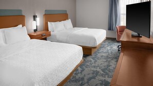 Une chambre d’hôtel avec deux lits, un bureau, une télévision et une fenêtre avec des rideaux.