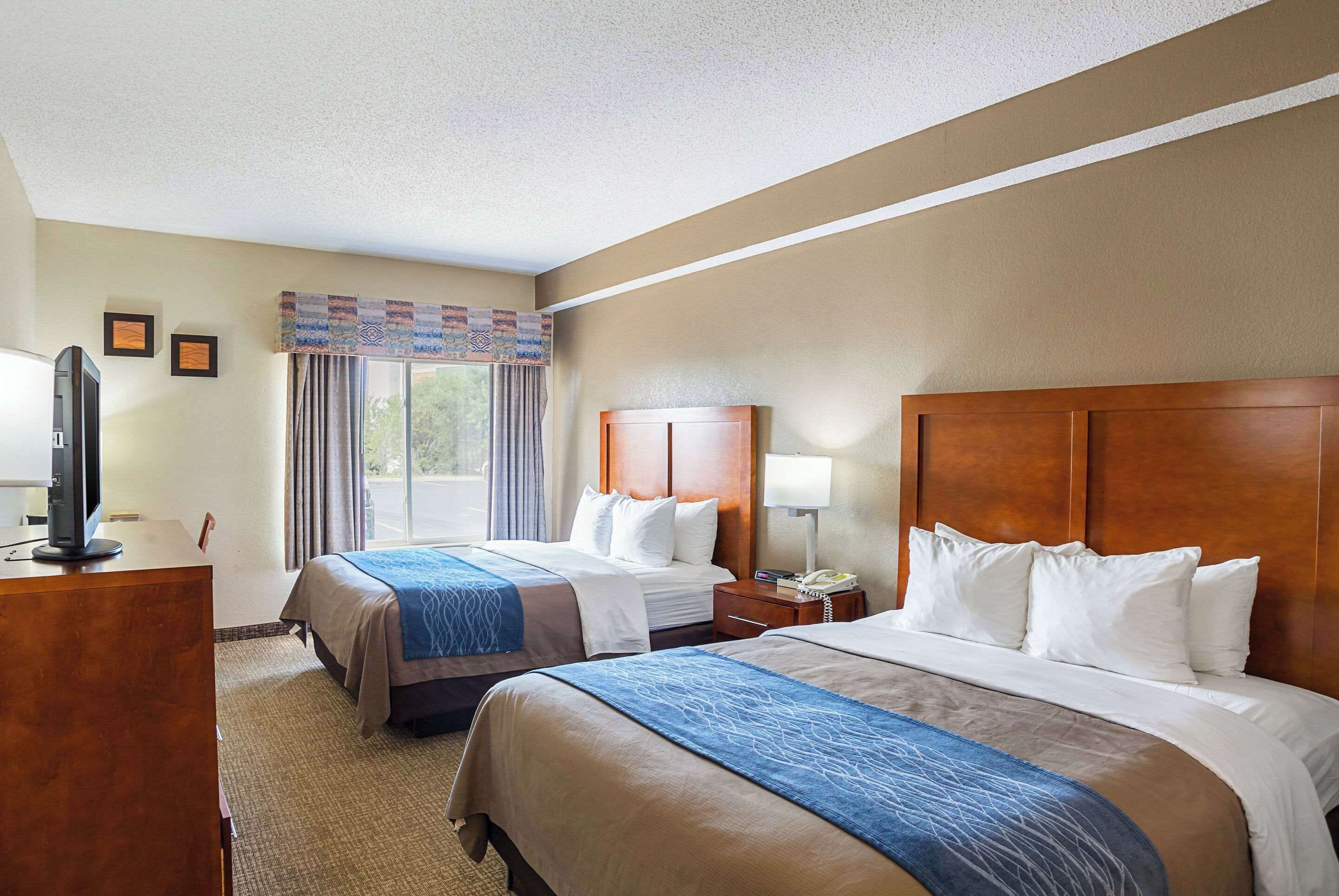 A hotel room with two beds, a desk, a TV, and a window with curtains.