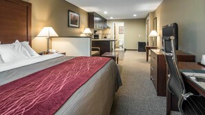 A hotel room with a bed, desk, chair, TV, and kitchenette.