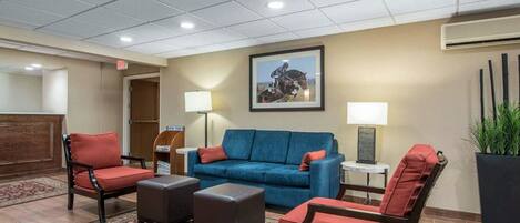 A lobby with a blue sofa, red armchairs, a patterned rug, and a framed picture on the wall.