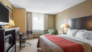 Habitación de hotel con cama, escritorio con televisor, silla, lámpara de escritorio y ventana con cortinas.