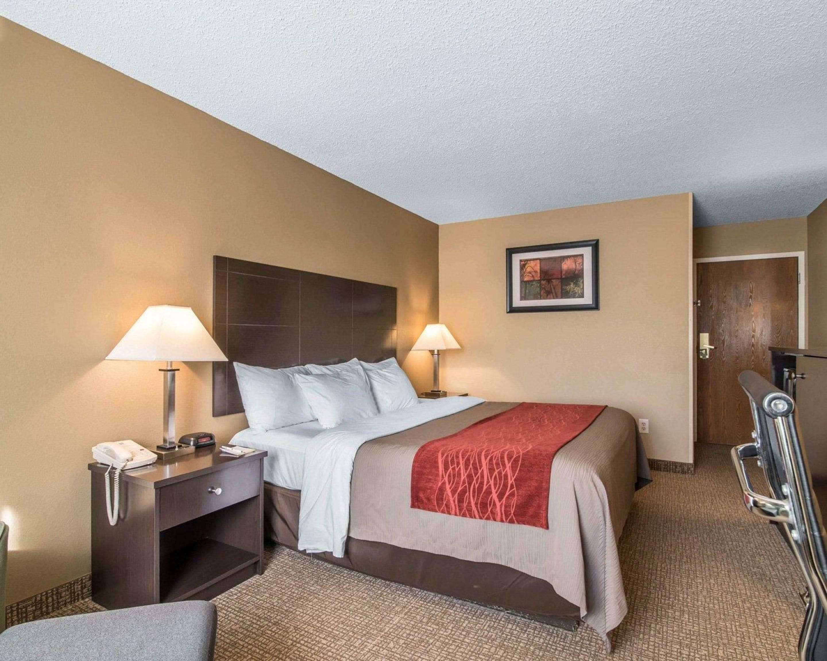 A hotel room with a bed, two bedside lamps, a telephone, a desk, and a door.