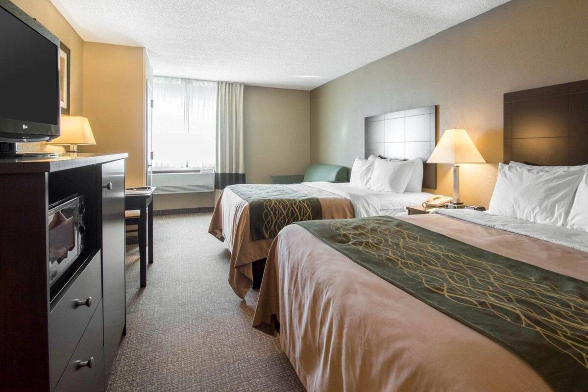 A hotel room with two beds, a TV, a desk, and a lamp.