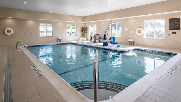 An indoor swimming pool with clear lane markings, a lifeguard chair, and a poolside area with a chair and table.