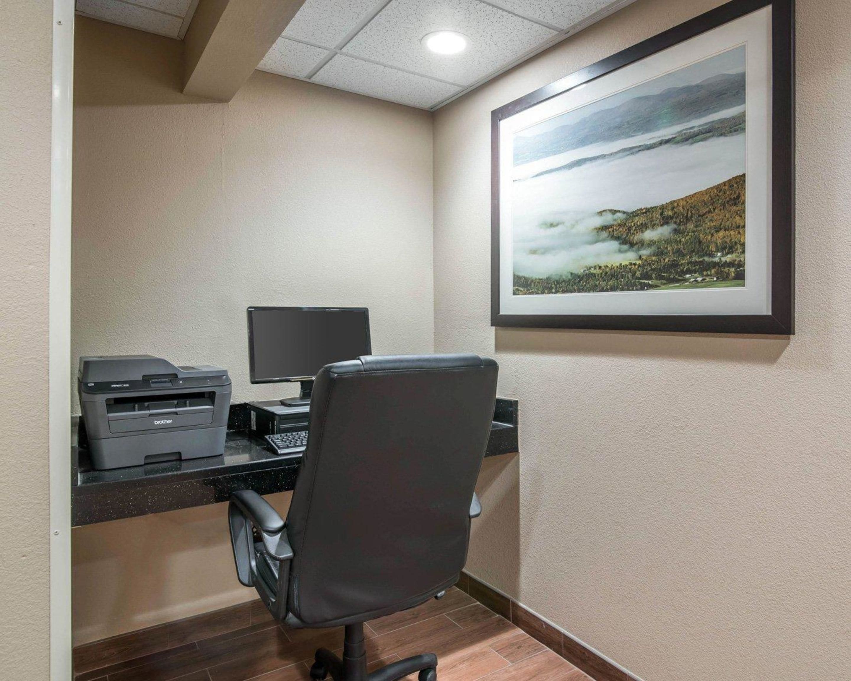 A workspace with a desk, computer, printer, and a framed landscape painting.