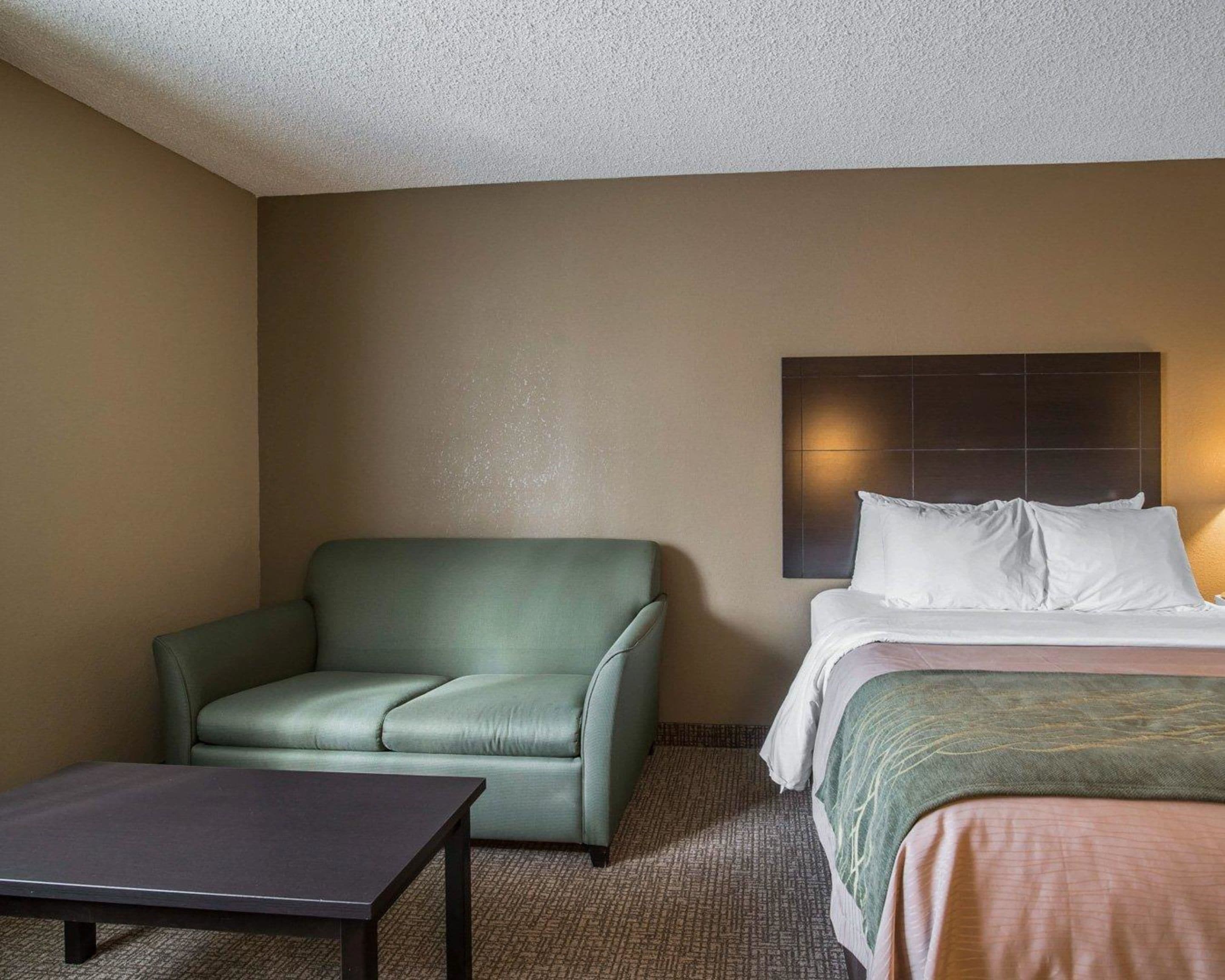 A hotel room with a green sofa, a bed with white linens, and a dark wooden table.